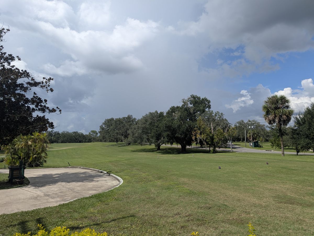 A golf fairway lined with live oaks under a sky full of clouds.