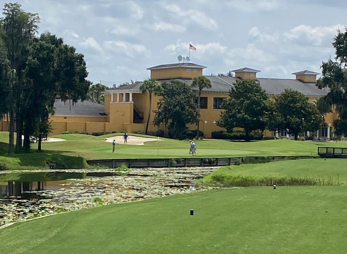 A golf clubhouse seen across a putting green, with a lily pond in the foreground.
